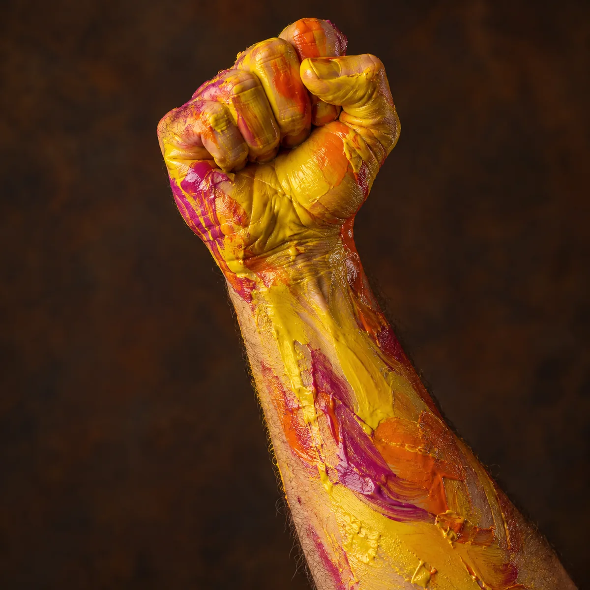 A raised forearm and fist covered in yellow and orange paint.